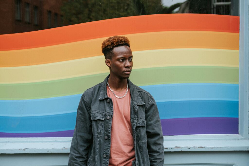 A person posing in front of a pride flag painting on a glass window